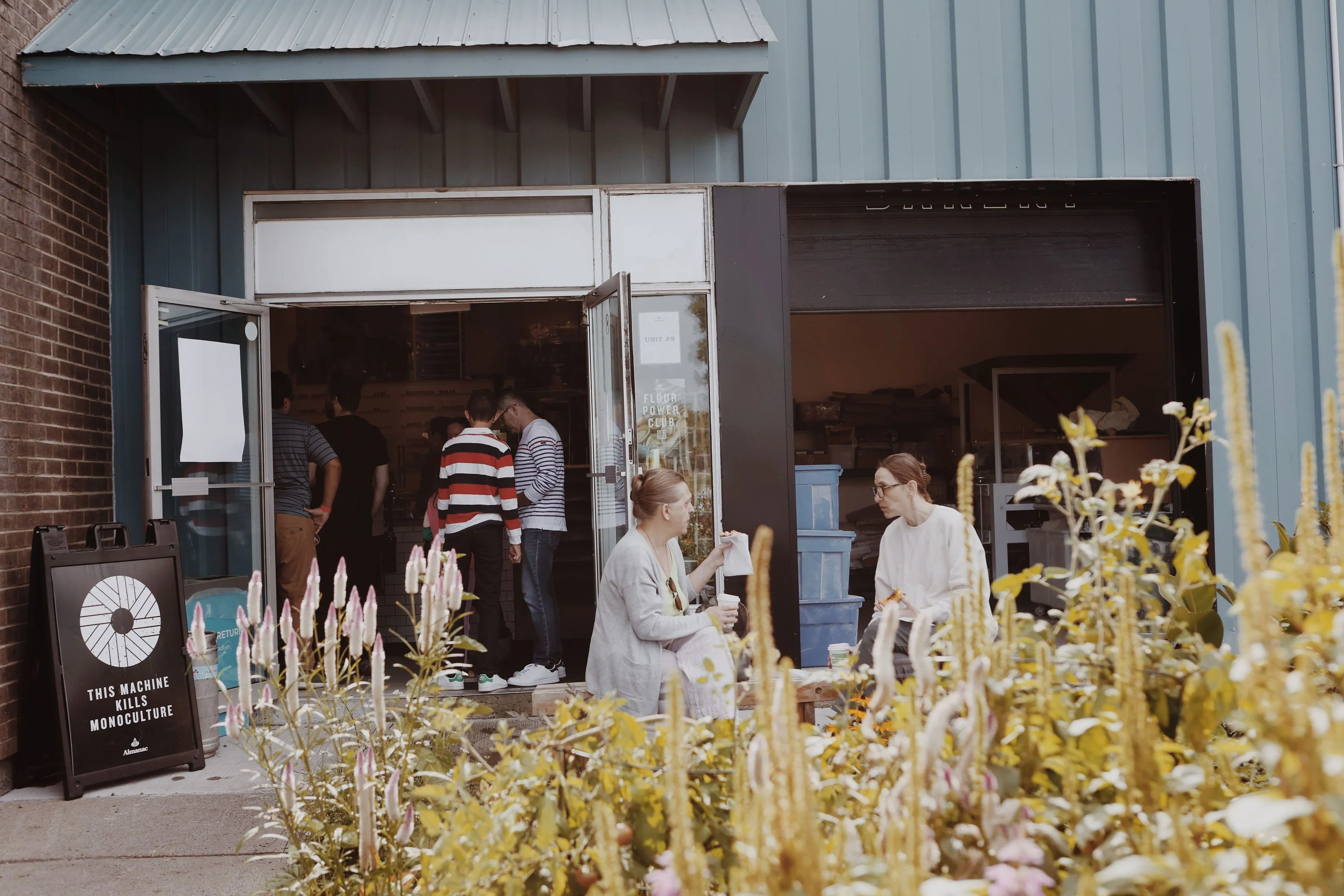 A picture of the front of Almanac Canotek with some people eating on the bench out front