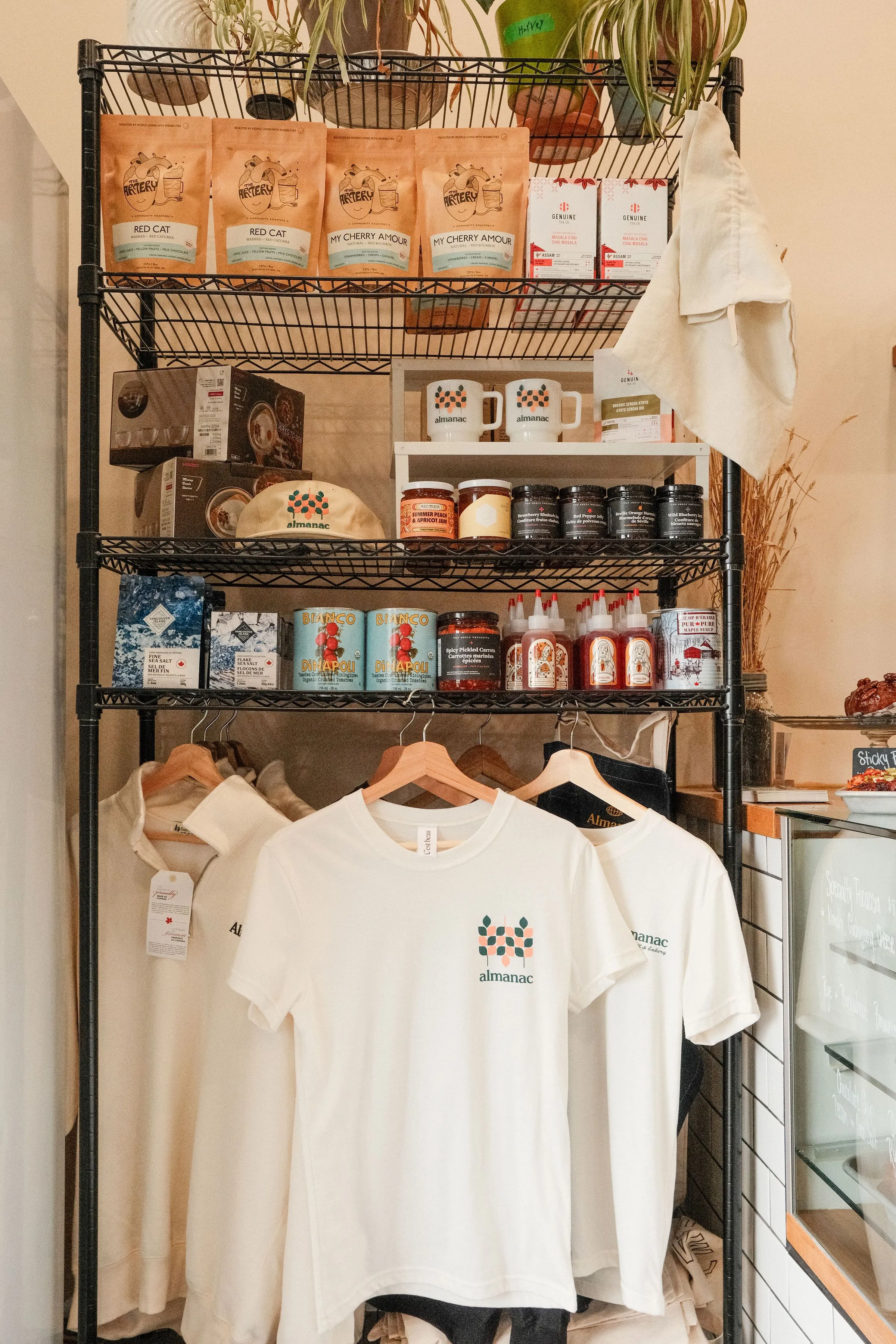 A retail shelf with t-shirts, coffee, hot honey etc being sold inside the bakery