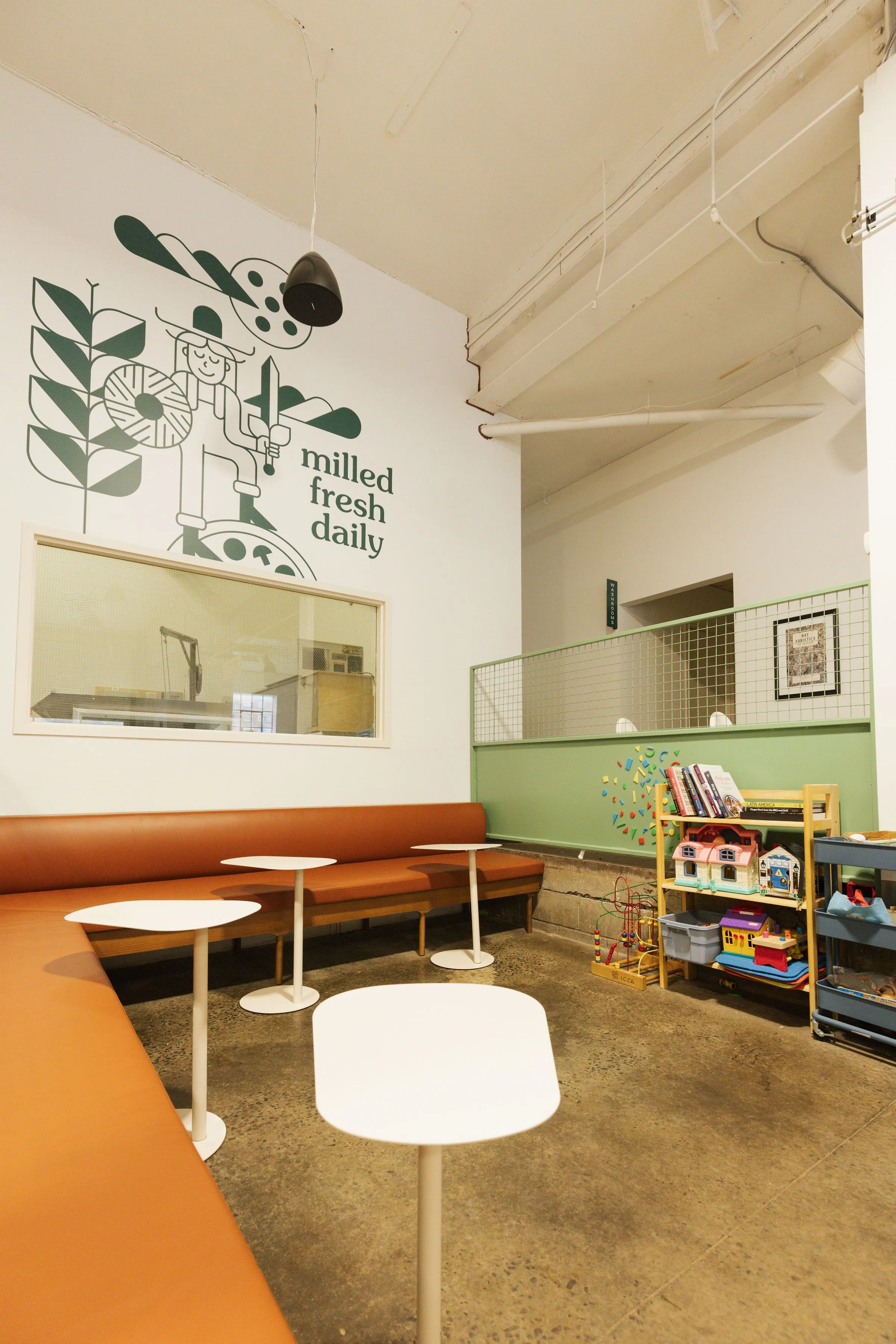 A view of the back of the cafe with benches and a window into the mill room and a little kids corner
